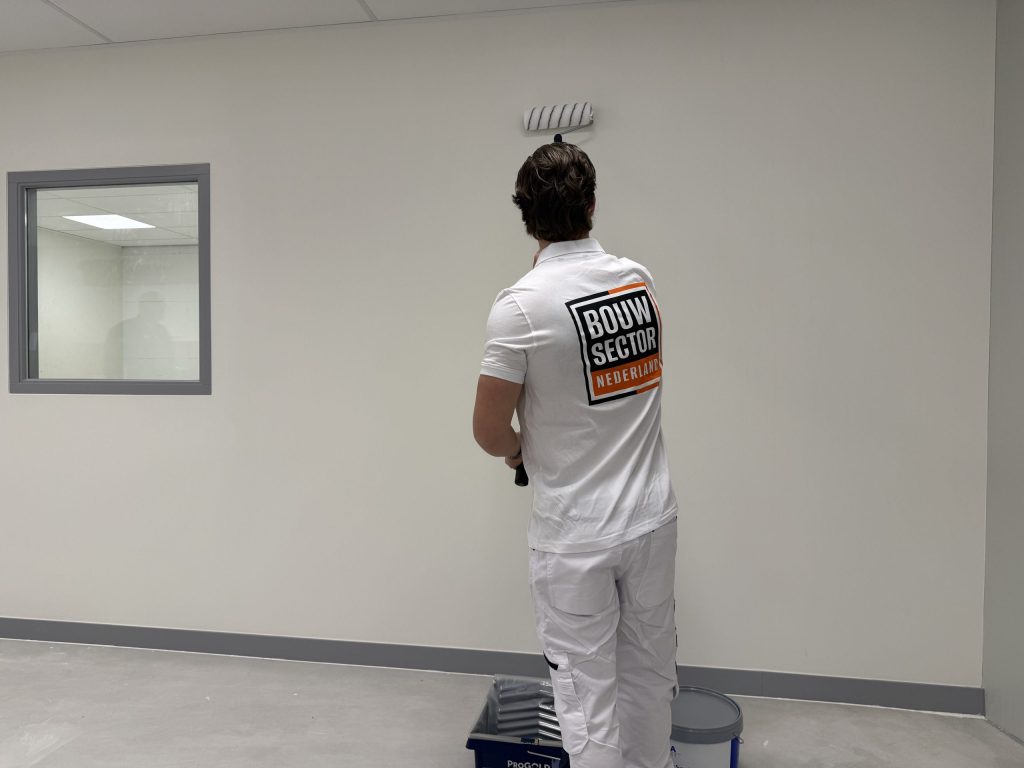 Schilder in witte werkkleding rolt een lichte wand in een ruimte met een binnenraam