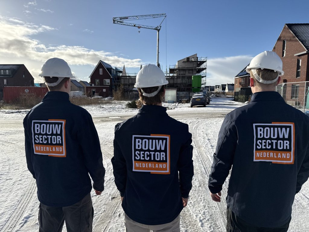 Drie vakmensen van Bouwsector Nederland met bouwhelm kijken naar huizen in aanbouw