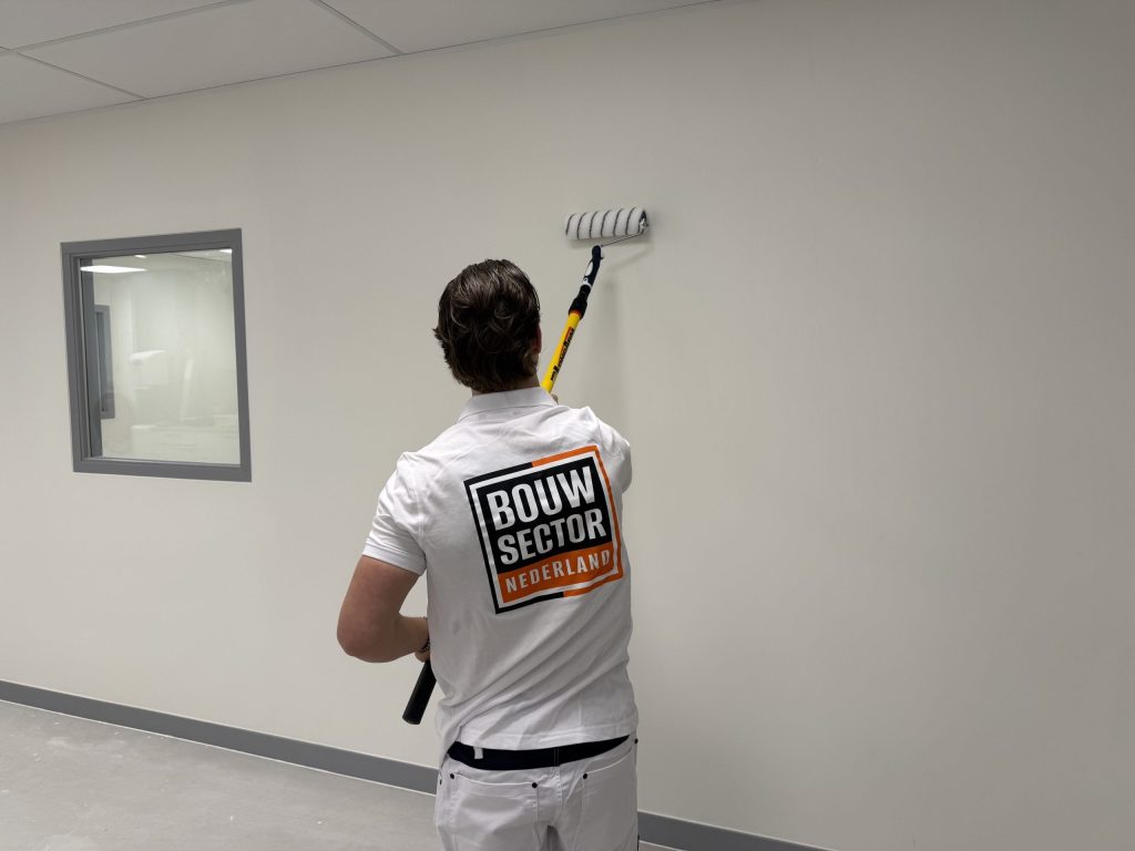 Schilder van Bouwsector Nederland zet muurverf op een witte wand met een roller aan een lange steel