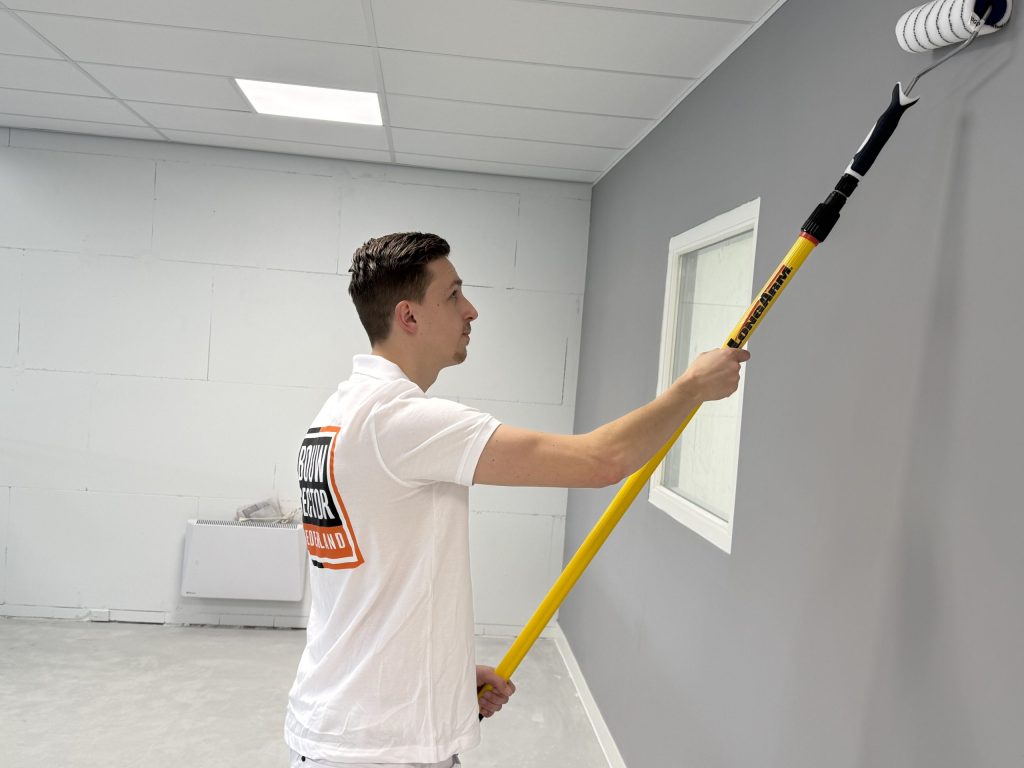 Schilder van Bouwsector Nederland rolt een grijze wand bij een raam, achter hem een nog kale muur