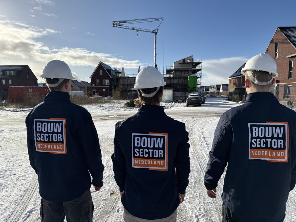 Medewerkers van Bouwsector Nederland met witte helm kijken naar een rij nieuwe woningen onder een blauwe lucht